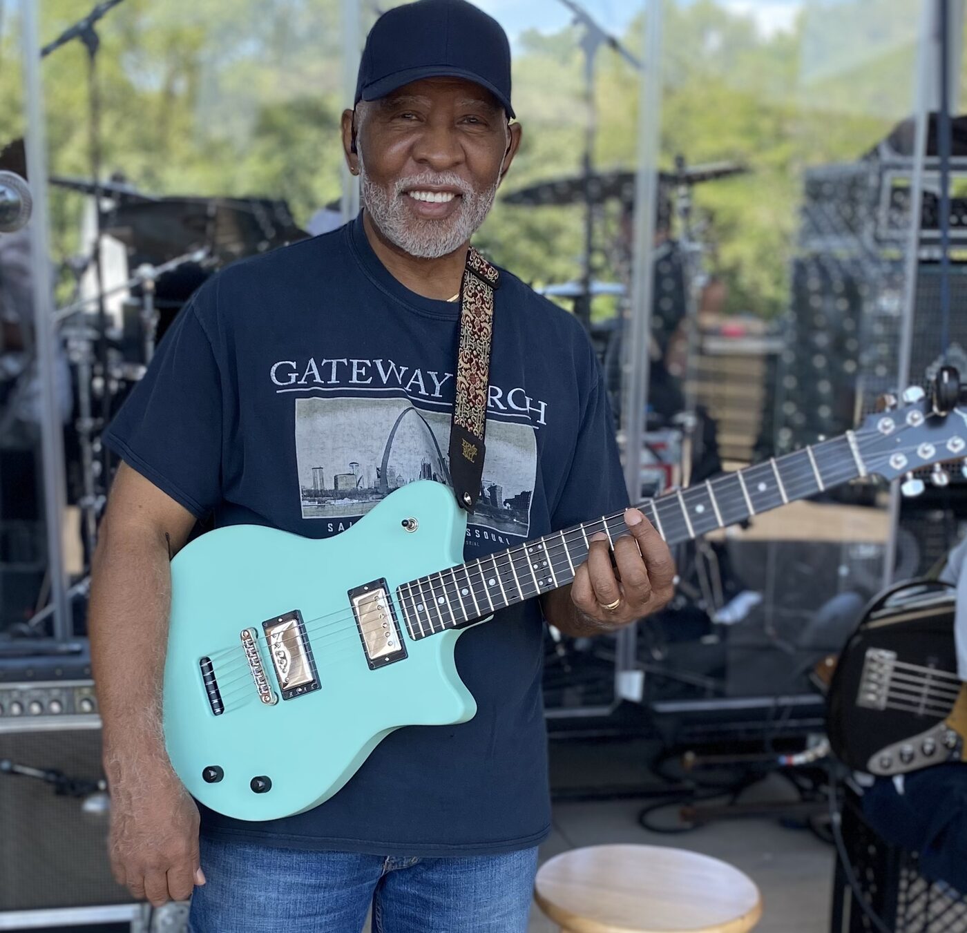 Boots Anderson smiling with a teal guitar outdoors